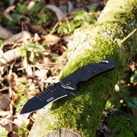 zwarte inklapbare mes met niet-zichtbaar lemmet op een met mos bedekt boomstamloze achtergrond
