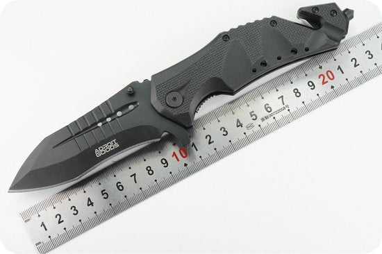 Zwart inklapbaar mes met gekarteld lemmet naast een metalen meetlat met rode cijfers.