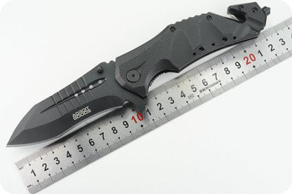 Zwart inklapbaar mes met gekarteld lemmet naast een metalen meetlat met rode cijfers.