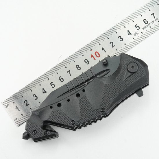 Opgevouwen zwarte zakmes met gegraveerd handvat naast een metalen liniaal van 15 cm