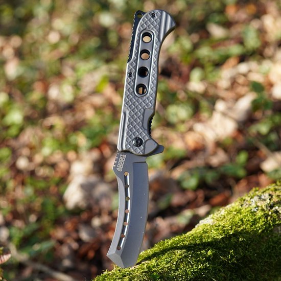 Zakmes met grijs handvat en gekartelde lemmetpunt in buitenomgeving op mossteek