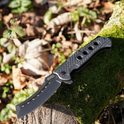 zwarte inklapbare mes met geperforeerd handvat liggend op een met mos bedekt boomstam