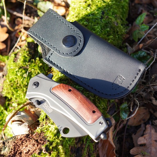 Opgevouwen zakmes met houten handvat naast zwart leren hoes op mosrijke bodem in natuur