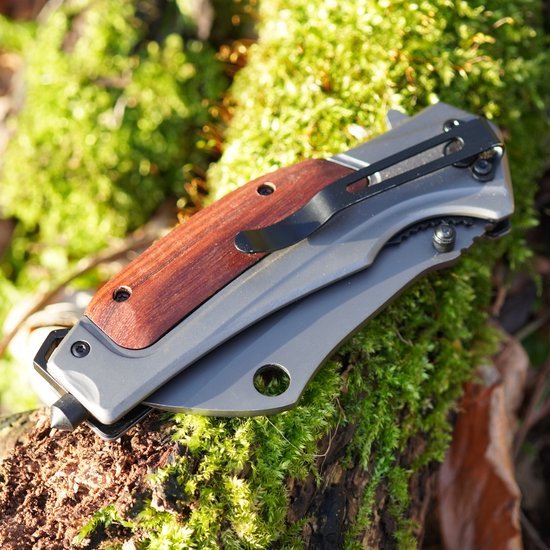 Opgevouwen zakmes met houten handvat en metalen clip liggend op mosgroene tak