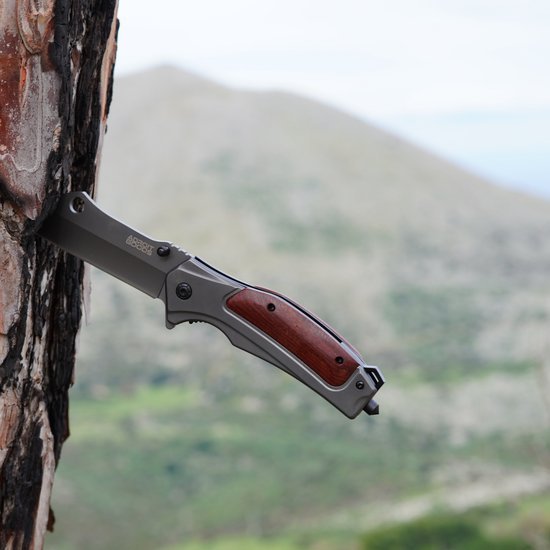 Openslaand zakmes met houten handvat vastgemaakt aan een boom met een wazige berg op de achtergrond