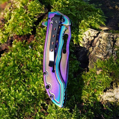 Opgevouwen metallic zakmes met iriserende kleuren liggend op groene mosgrond en boomschors