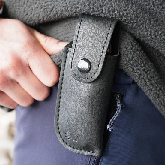 Hand die een zwart leren hoesje met drukknop aan een broekriem bevestigt.