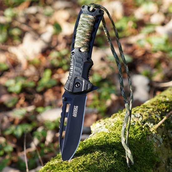 Zwart jachtmes met kartelrand en camouflagetouw op een groene mosachtige boomstam.