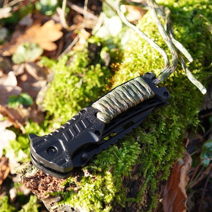 zwarte inklapbare zakmes met camouflage handgreep op mos bedekte boomstam in bos