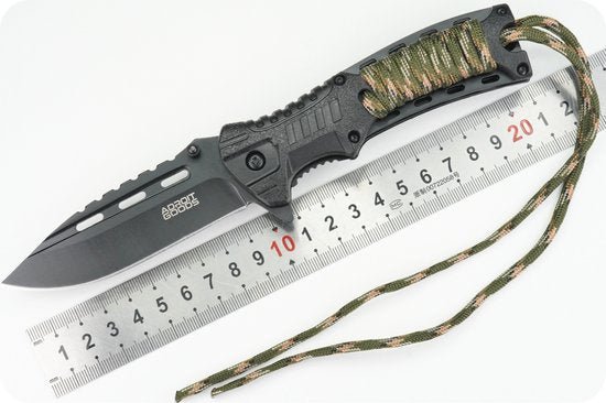 zwarte mes met gekarteld lemmet en camouflage koord naast metalen liniaal