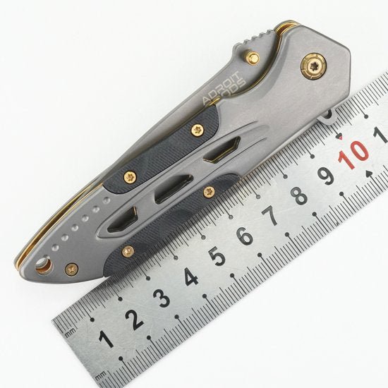 gevouwen metallic zakmes met gouden accenten naast een metalen liniaal op witte achtergrond