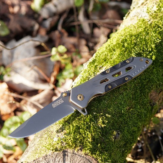 Vouwmes met metalen handgreep en scherp mes liggend op met mos bedekt hout in buitenomgeving