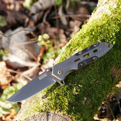 Vouwmes met metalen handgreep en scherp mes liggend op met mos bedekt hout in buitenomgeving