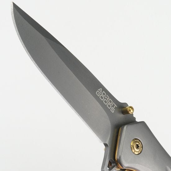Close-up van een scherp grijs mes met metalen handvat en Adroit Goods logo zichtbaar