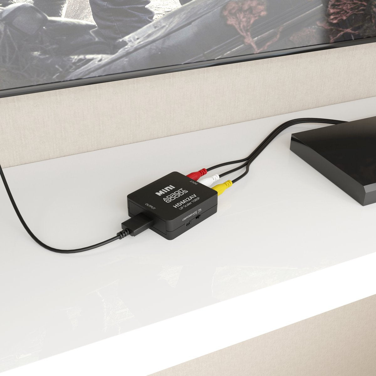 Kleine zwarte audio-video converter aangesloten met rode, witte en gele kabels op witte kast