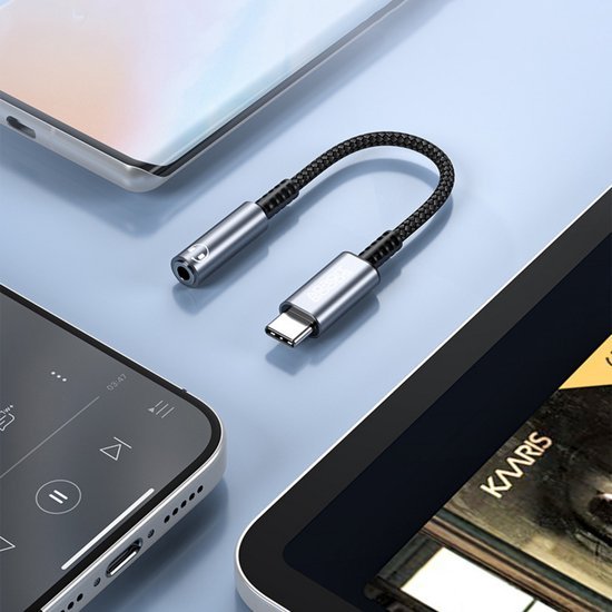 Zwarte gevlochten USB-C naar 3,5 mm hoofdtelefoonadapter op lichtblauwe ondergrond naast apparaten