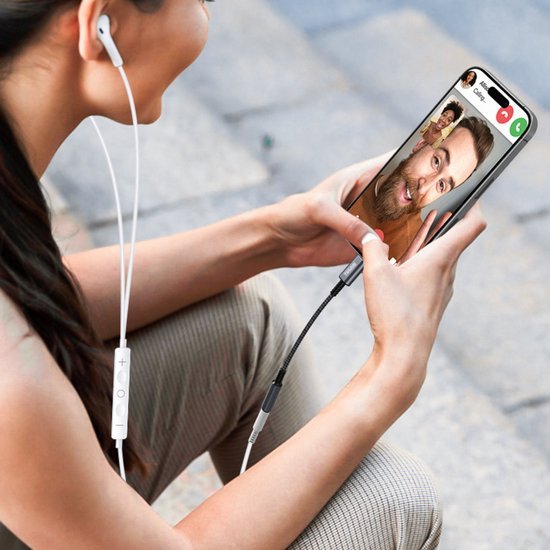 Vrouw met oordopjes voert videogesprek op smartphone tijdens buiten zitten op stenen vloer.