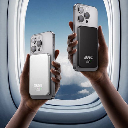 Twee handen houden telefoons vast met zwarte en zilveren powerbanks voor vliegtuigraam.