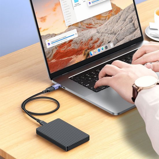 Handen typen op laptop met aangesloten zwart draagbaar extern opslagapparaat op houten tafel