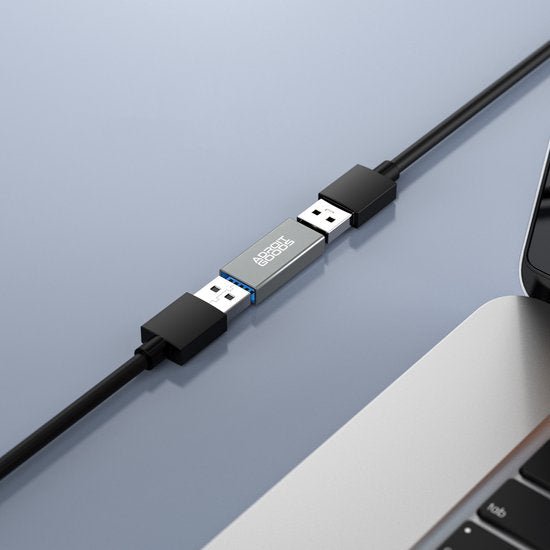 Twee zwarte USB-kabels verbonden met een zilveren AdroitGoods adapter tussen een laptop en andere kabel
