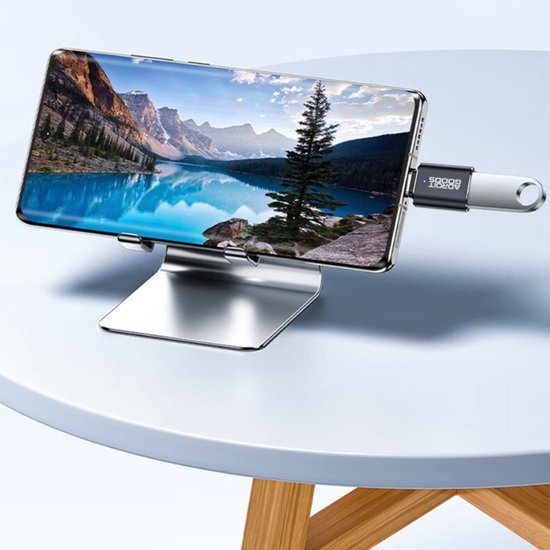 Mobiele telefoon met berglandschap op scherm, geplaatst op een stijlvol metalen standaardhouder.