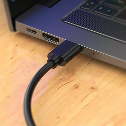 Zwarte USB-kabel die is aangesloten op een laptop met een houten ondergrond eronder