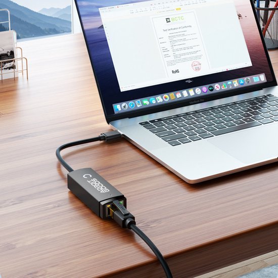 Laptop verbonden met een netwerkadapter op een houten bureau bij een raam met uitzicht op bergen