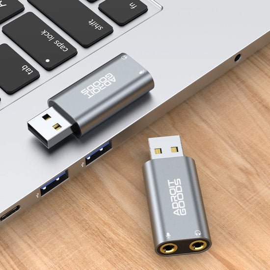 Twee zilverkleurige USB-adapters van AdroitGoods, één aangesloten op een laptop, geplaatst op een houten oppervlak