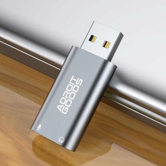 Zilverkleurige USB-adapter met AdroitGoods-logo, geplaatst op houten oppervlak naast laptop