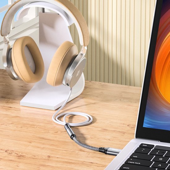 Beige over-ear koptelefoon aangesloten op een laptop op een houten bureau met standaard.