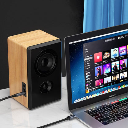 Houten luidspreker met zwarte voorkant naast een laptop met muziekapp op een bureau