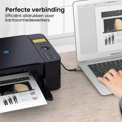 Een hand bedient een laptop die verbonden is met een printer die documenten afdrukt op een bureau.