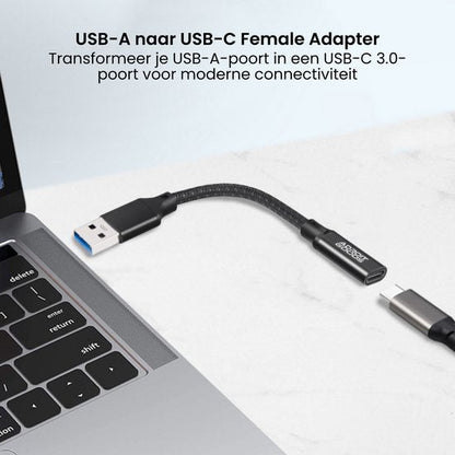 Zwarte USB-A naar USB-C adapterkabel aangesloten op een zilveren laptop op een witte ondergrond