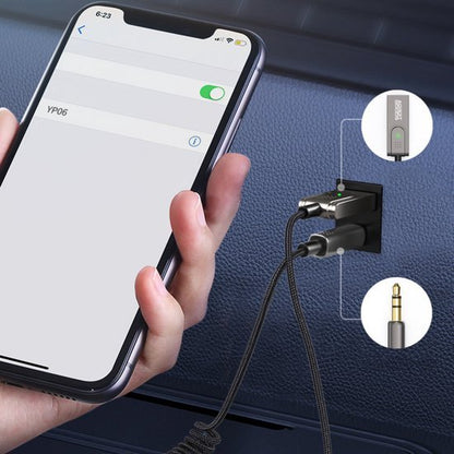 Close-up van hand met smartphone verbonden via adapter en 3,5 mm audio kabel in autoport