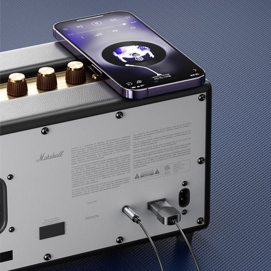 Smartphone speelt muziek via bedrade verbinding op grijze Marshall versterker met knoppen bovenop