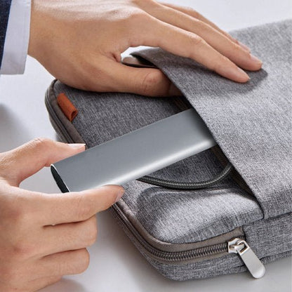 Hand stopt een grijs apparaat in een grijze stoffen tas met ritssluiting op een witte ondergrond.