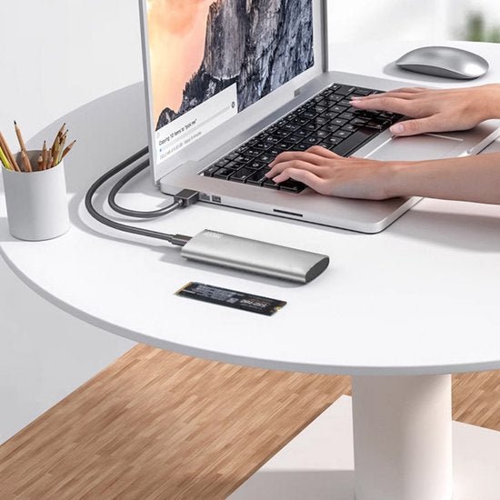 Handen typen op laptop die verbonden is met een externe hub op een witte ronde tafel