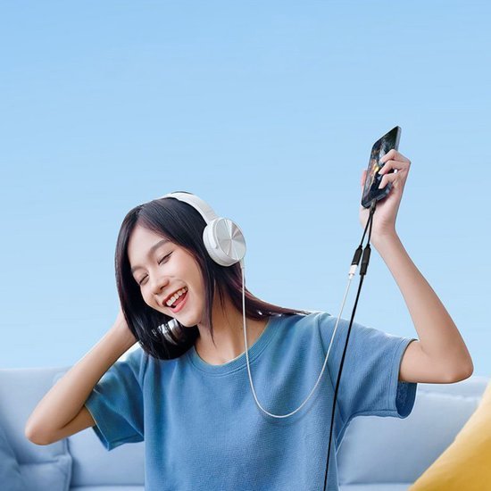 Vrolijke jonge vrouw met witte koptelefoon die naar muziek luistert via smartphone in blauwe kamer.