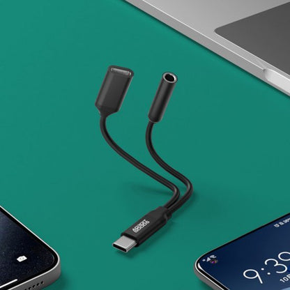 Zwarte adapterkabel met USB-C naar 3,5mm audio en oplaadpoort naast telefoons en laptop