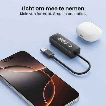 Compact zwarte USB-adapter met kabel naast smartphone en witte oordopjes op blauwe achtergrond