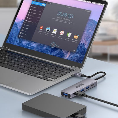 Laptop met aangesloten hub en externe harde schijf op een lichtgrijze tafel in moderne kamer