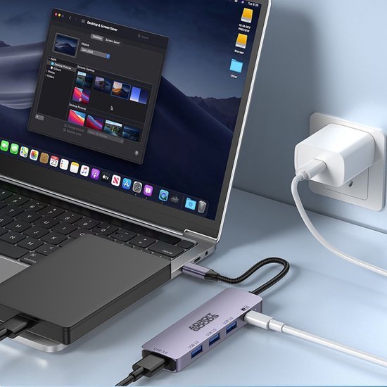 Lichte laptop met aangesloten meerdere kabels en een grijze hub naast een muurstekker.