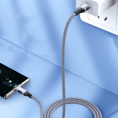 Grijze gevlochten oplaadkabel verbonden met een telefoon en een wandcontactdoos in een blauwe omgeving