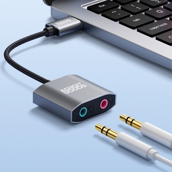 grijze usb adapter met audiopoorten aangesloten op laptop met audiokabels ernaast