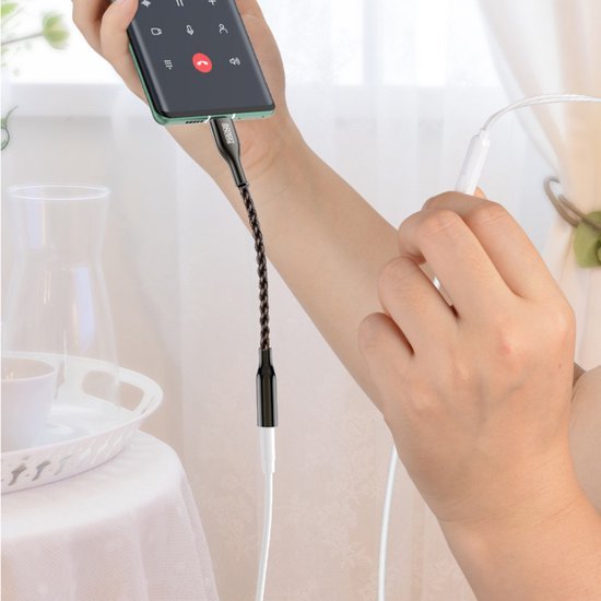 Hand die een telefoon vasthoudt met een aangesloten zwarte audio-adapterkabel en witte oortjes