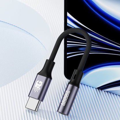 Zwarte gevlochten USB-C naar 3,5 mm audio-adapter naast een smartphone met blauw scherm