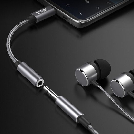 Zilverkleurige oordopjes met kabel en adapter aangesloten op een smartphone op zwarte achtergrond