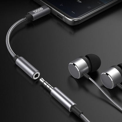 Zilverkleurige oordopjes met kabel en adapter aangesloten op een smartphone op zwarte achtergrond