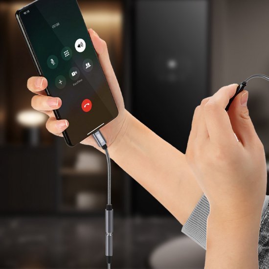 Hand houdt smartphone met telefoongesprek en een oortelefoonaansluiting in een woonkameromgeving