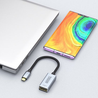 Zilverkleurige adapter met USB-C naar DisplayPort kabel naast laptop en kleurrijke smartphone.